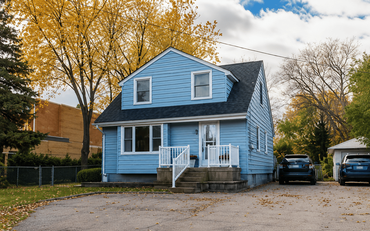 Blue two-story house with a dormer and small front porch, framed by autumn trees.