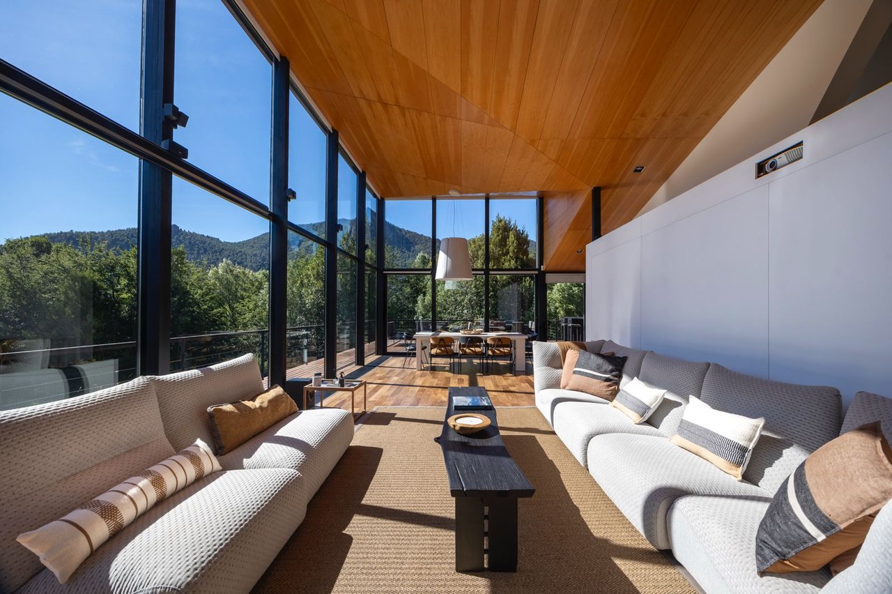 Living room with floor-to-ceiling windows, pale sofas, and wooded mountain views.