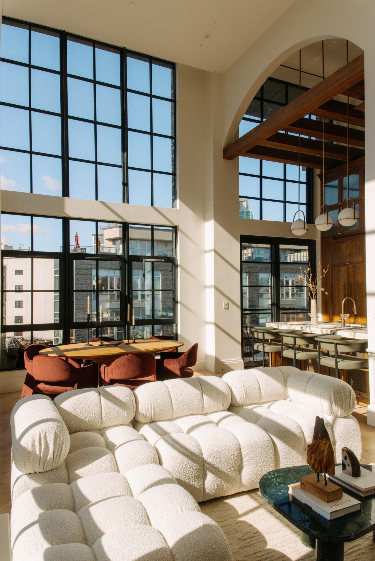 Double-height living and dining area with tall grid windows, a white sectional, and exposed wood beams.