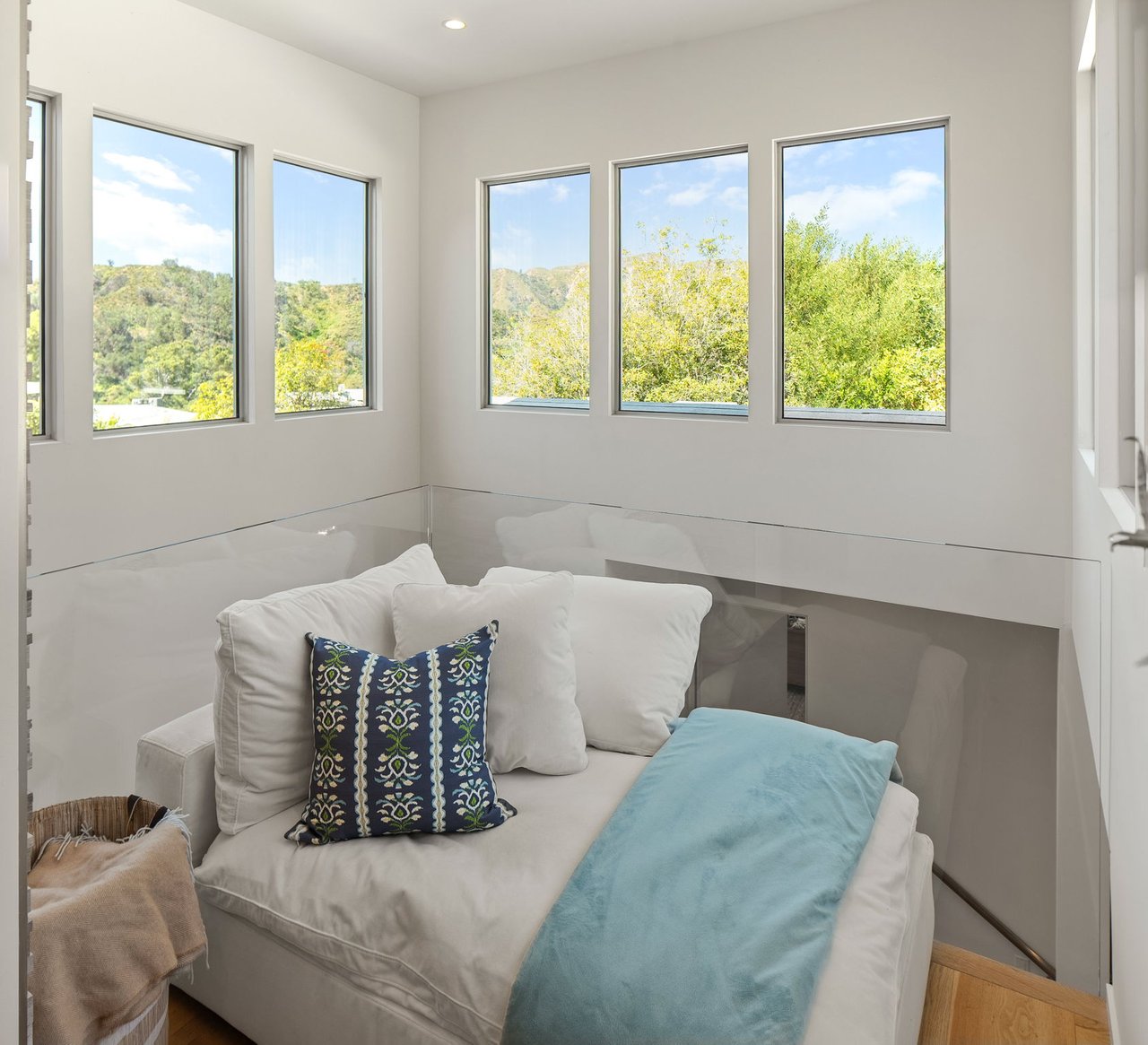 Sitting area with a white sectional sofa, turquoise throw, and tall windows overlooking green hills.
