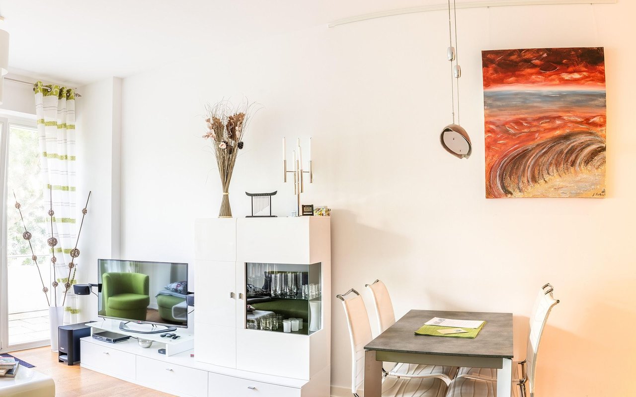Bright living and dining room with a white display cabinet, green armchair, and large abstract painting.