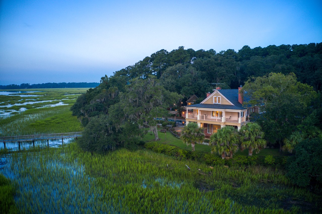 Coastal home beside a grassy tidal marsh, with a boardwalk crossing the foreground at dusk.