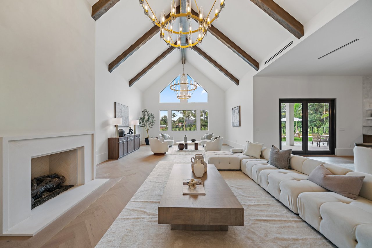 Vaulted living room with exposed wood beams, gold chandeliers, fireplace, and white sectional seating.
