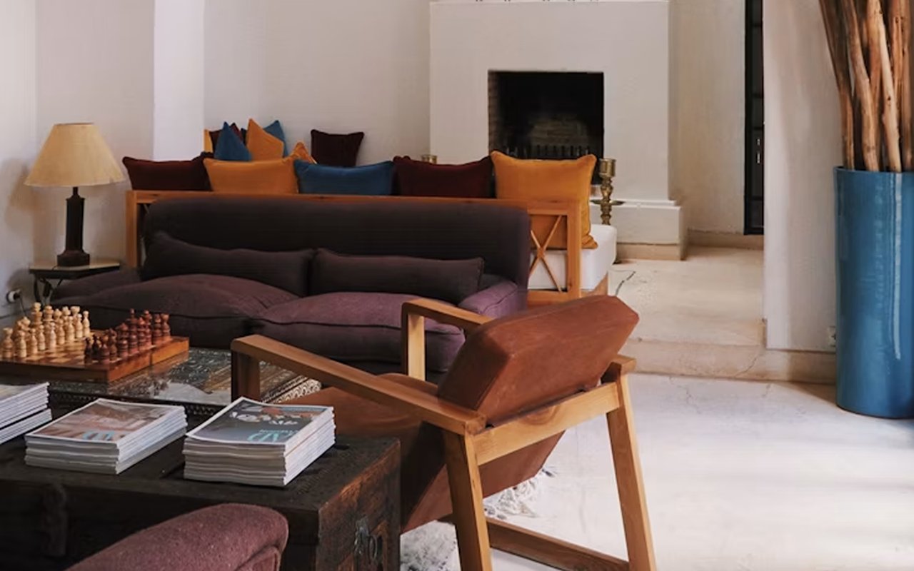 Furnished living room with a fireplace, colorful cushions, a wooden lounge chair, and chess pieces.