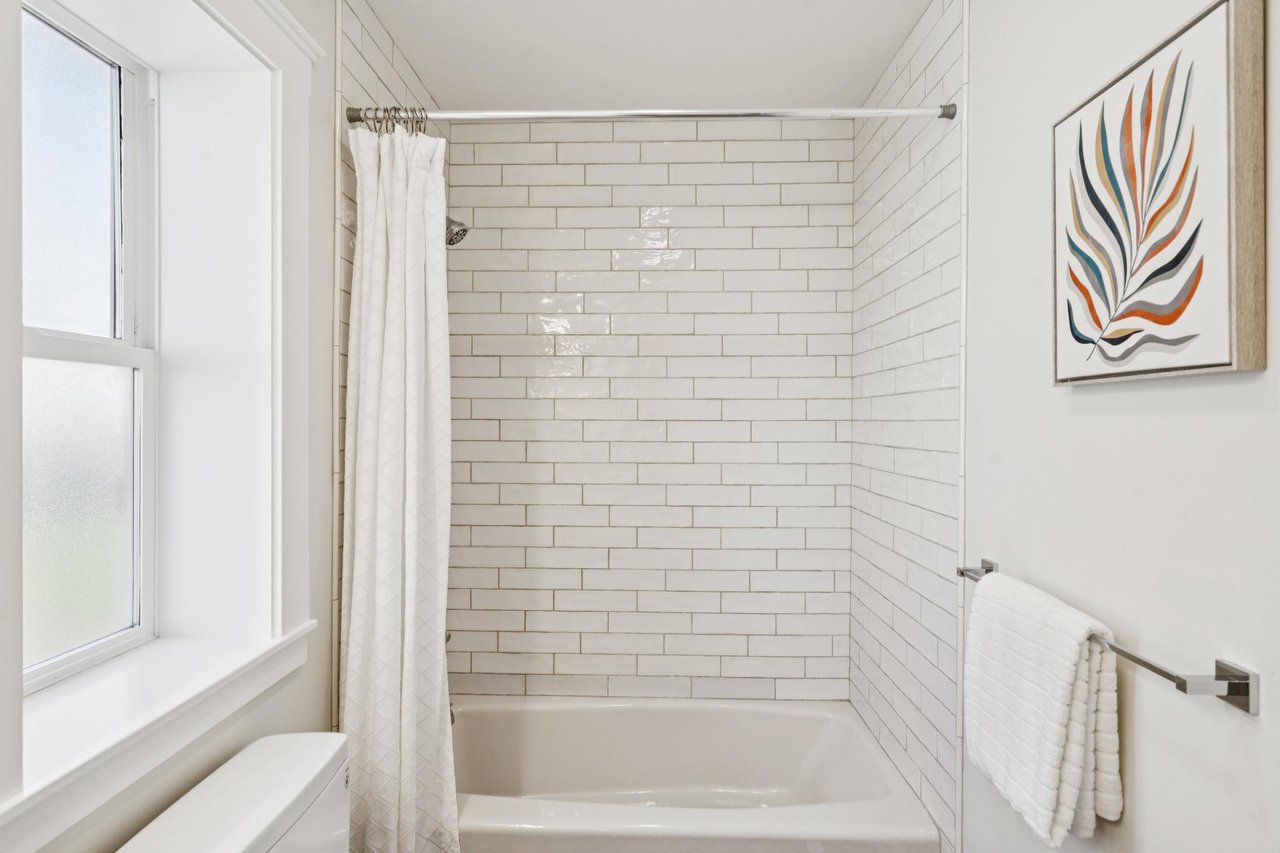 Bathroom with a white subway-tile tub and shower beside a large window.