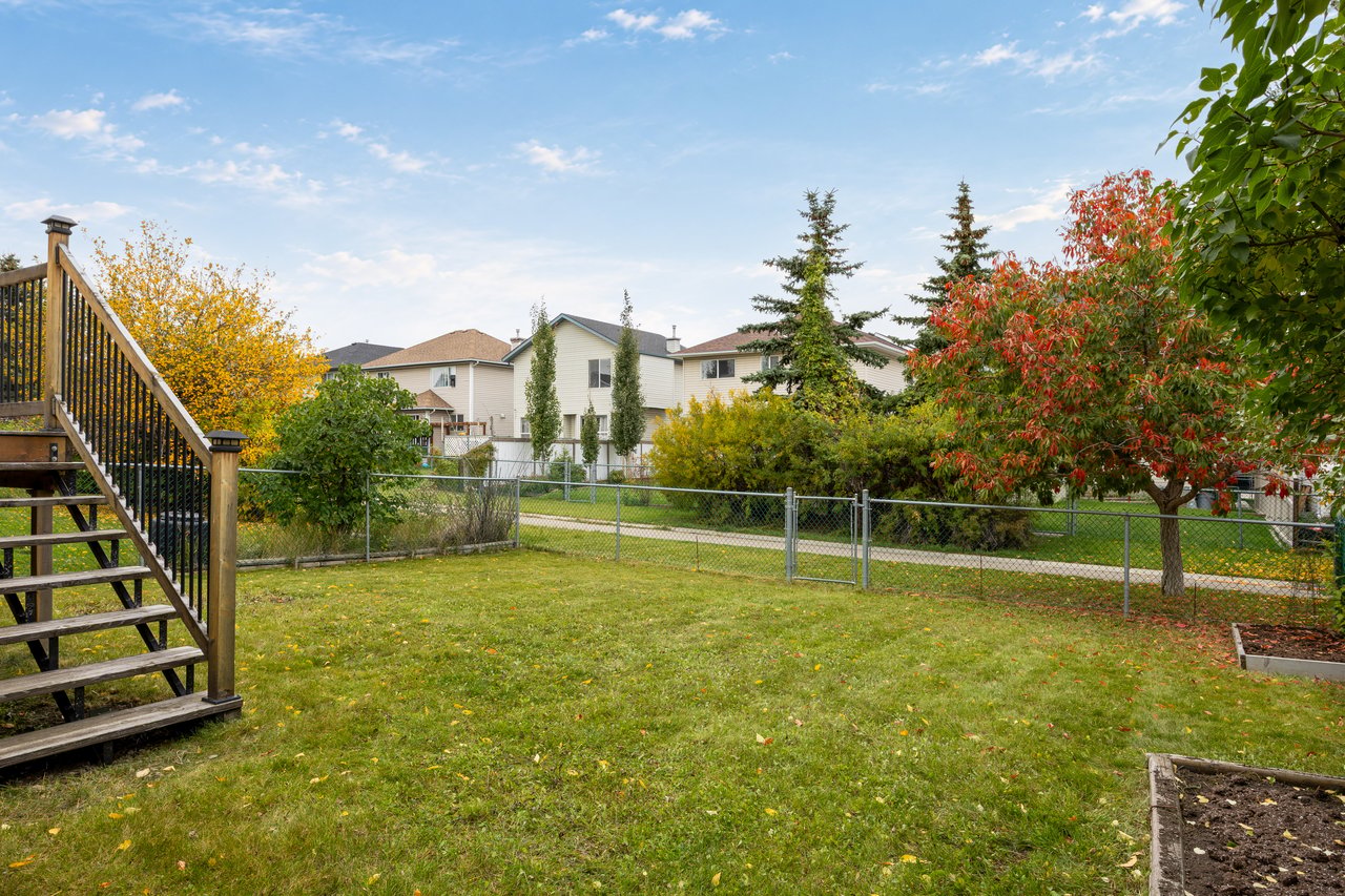 Backyard with a fenced lawn, wooden deck stairs, and autumn-colored trees.