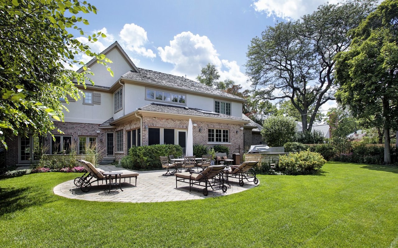 Home’s brick-and-siding rear exterior with a furnished stone patio and spacious green lawn.