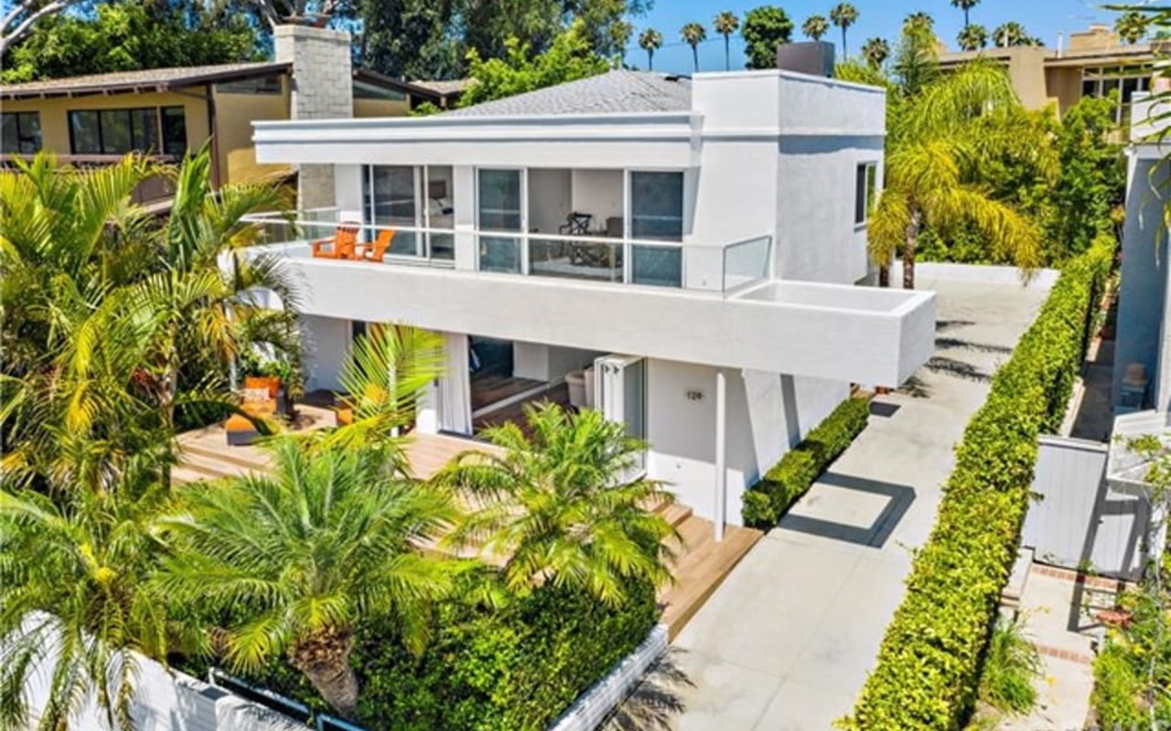 Modern white two-story house with glass-railed balconies and a palm-lined driveway.