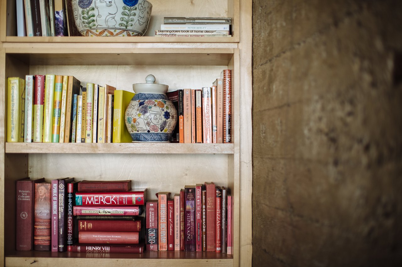 Built-in wooden bookshelf with colorful books and patterned ceramic jars beside a textured wall.
