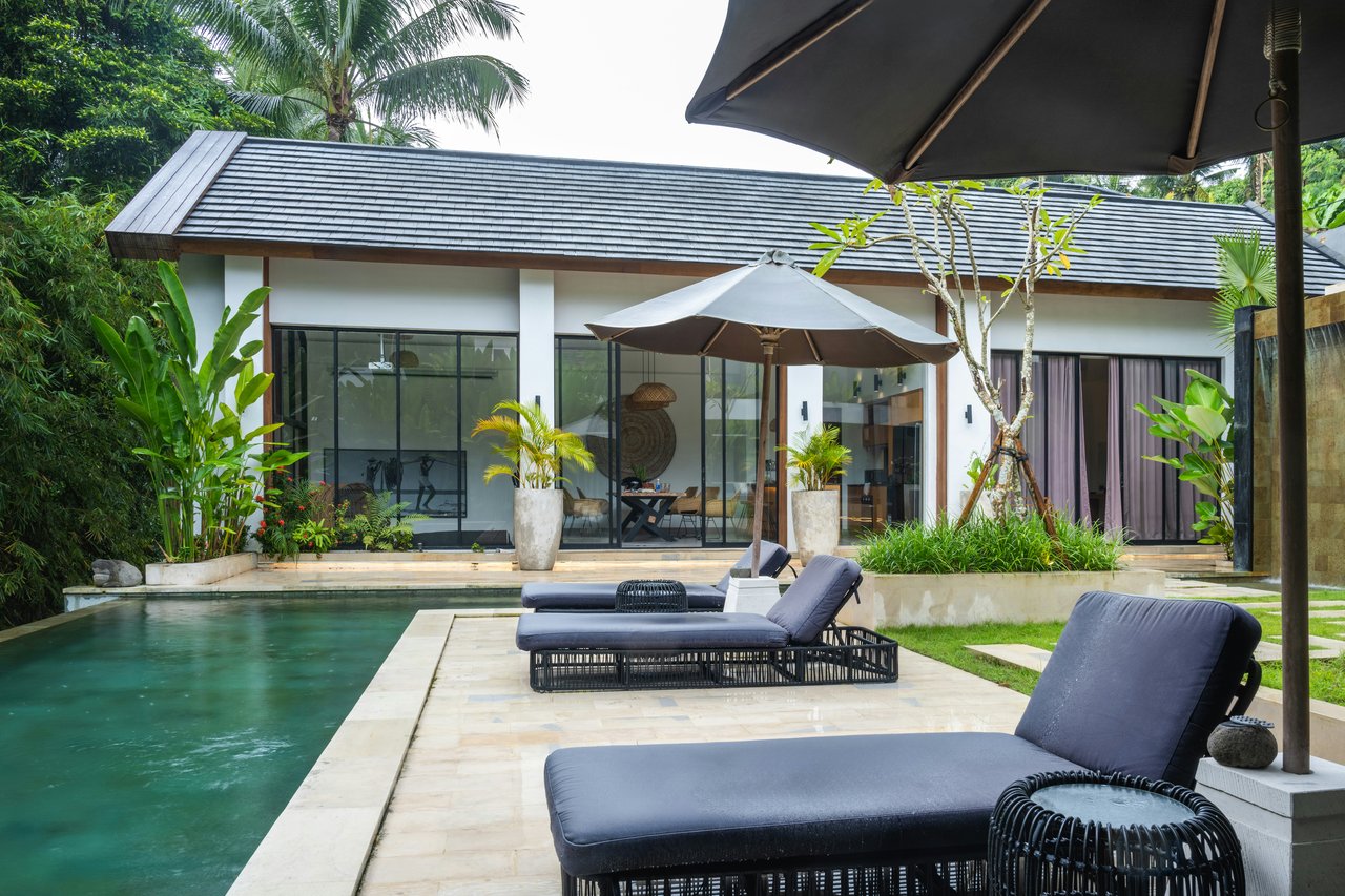 Modern white house beside a swimming pool, with cushioned loungers and tropical landscaping.