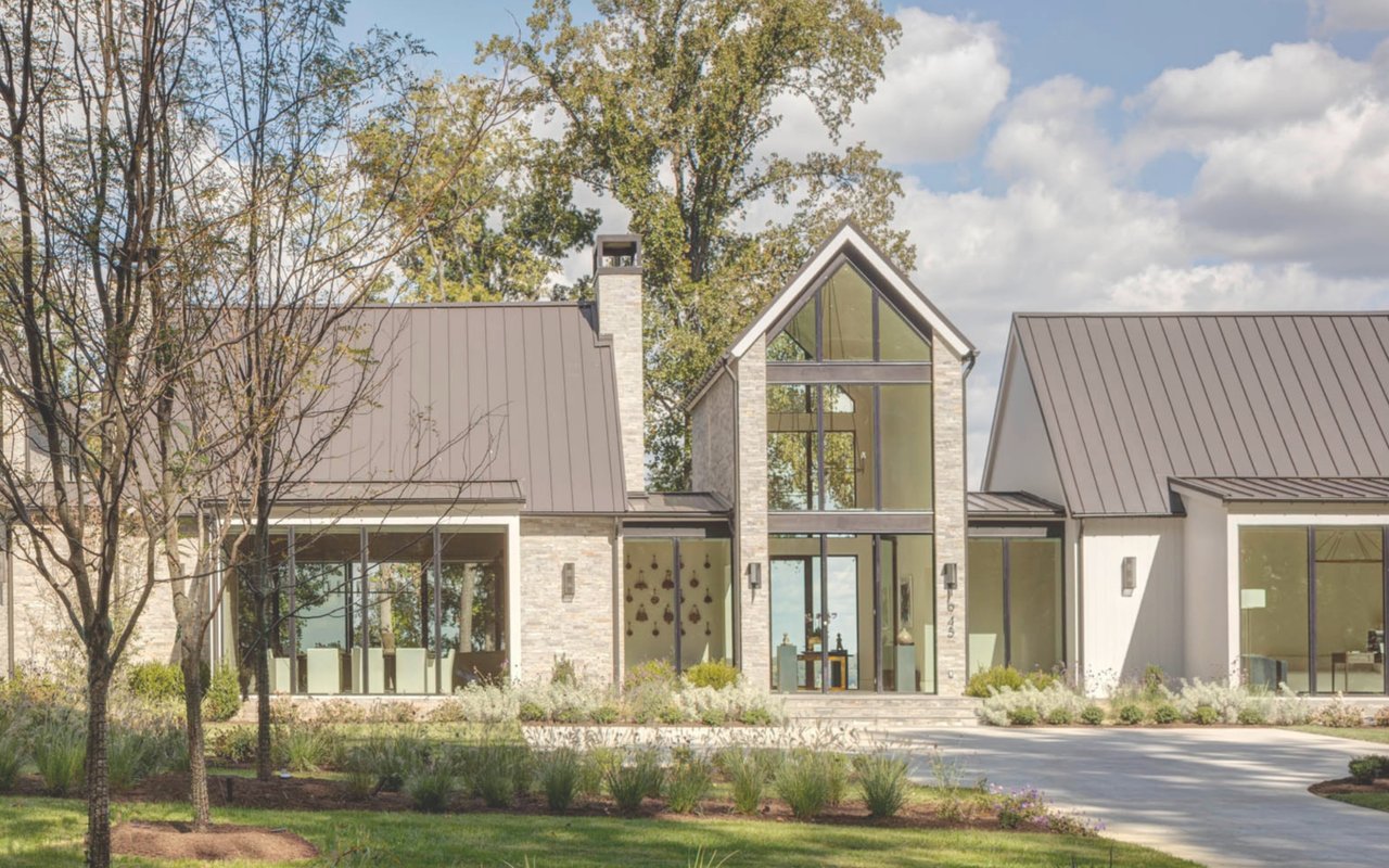 Contemporary stone house with a tall glass entry, metal roofs, and landscaped grounds.