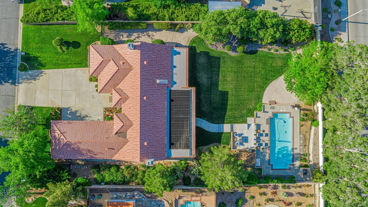 Aerial view of a tile-roofed home with solar panels, green lawn, and backyard swimming pool.