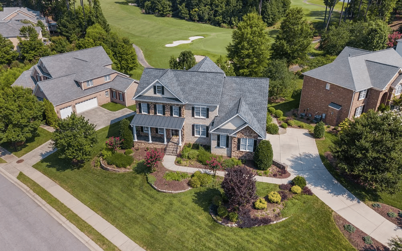 Aerial view of a brick home with landscaped gardens beside a golf course.