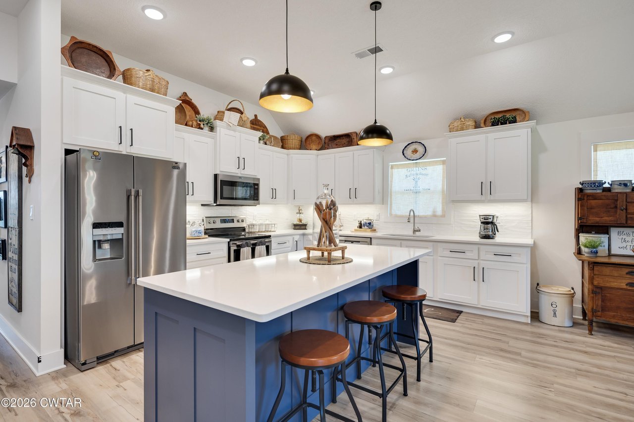 Bright kitchen with white cabinets, stainless appliances, and a blue island with bar stools.