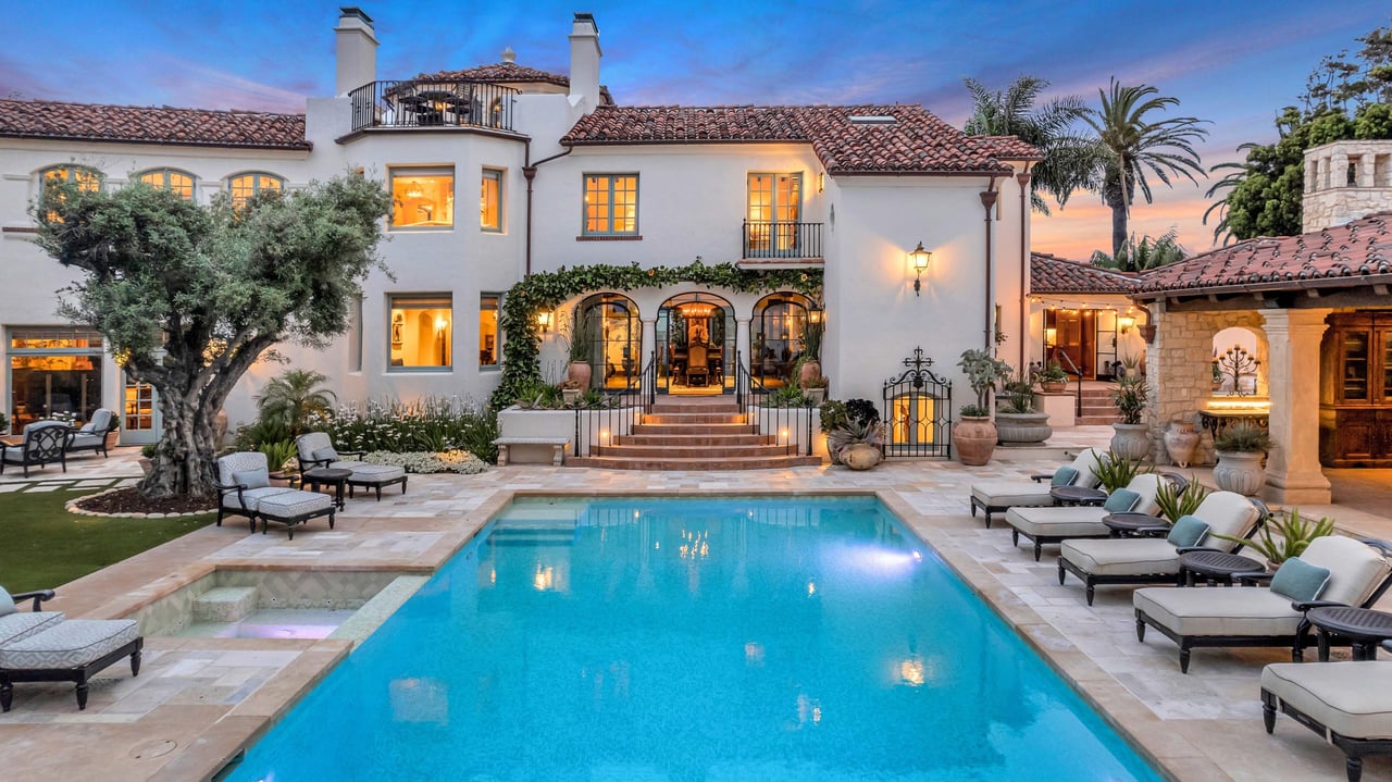 White stucco home with a red tile roof overlooking a courtyard pool at dusk.