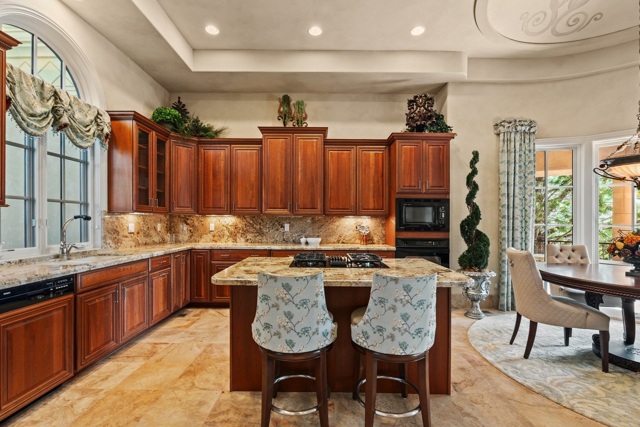 Kitchen with a large cooktop island, rich wood cabinetry, and an arched window above the sink.