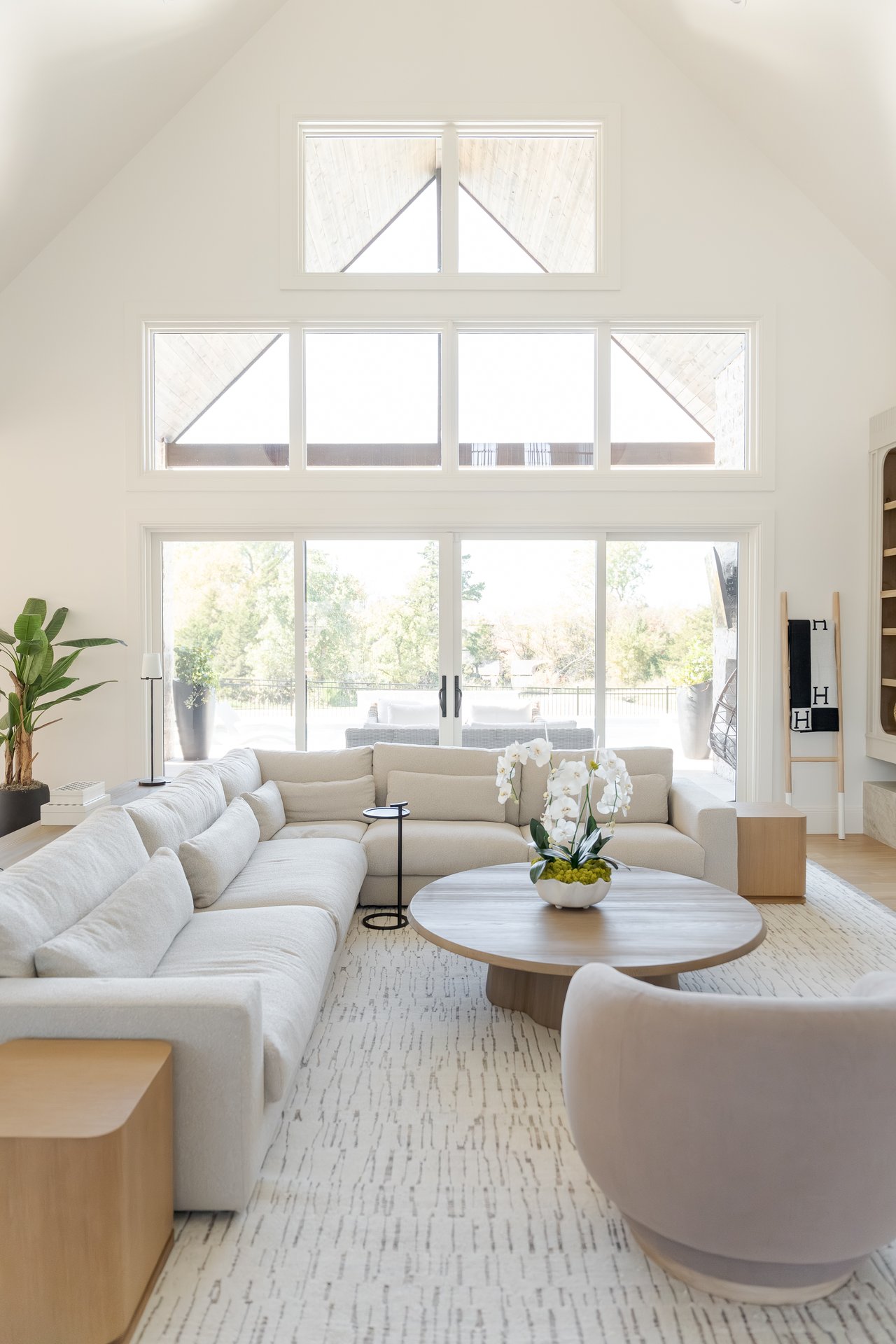 Spacious open-concept living room with soaring two-story floor-to-ceiling windows overlooking a luxury pool and greenbelt in Edmond, Oklahoma — offering breathtaking sunset views and elegant modern design.