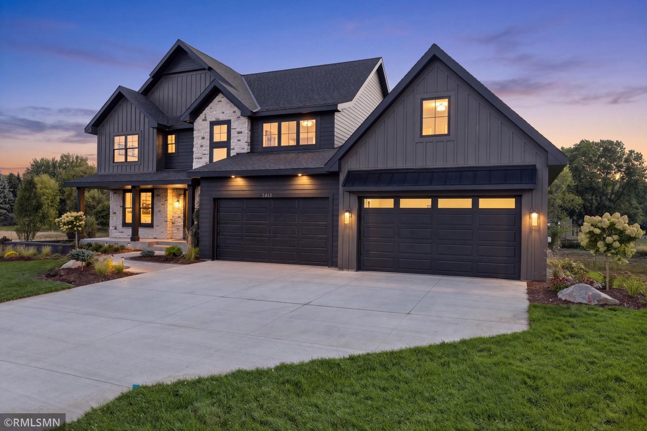 Two-story gray house with stone accents, four-car garage, and wide driveway at dusk.