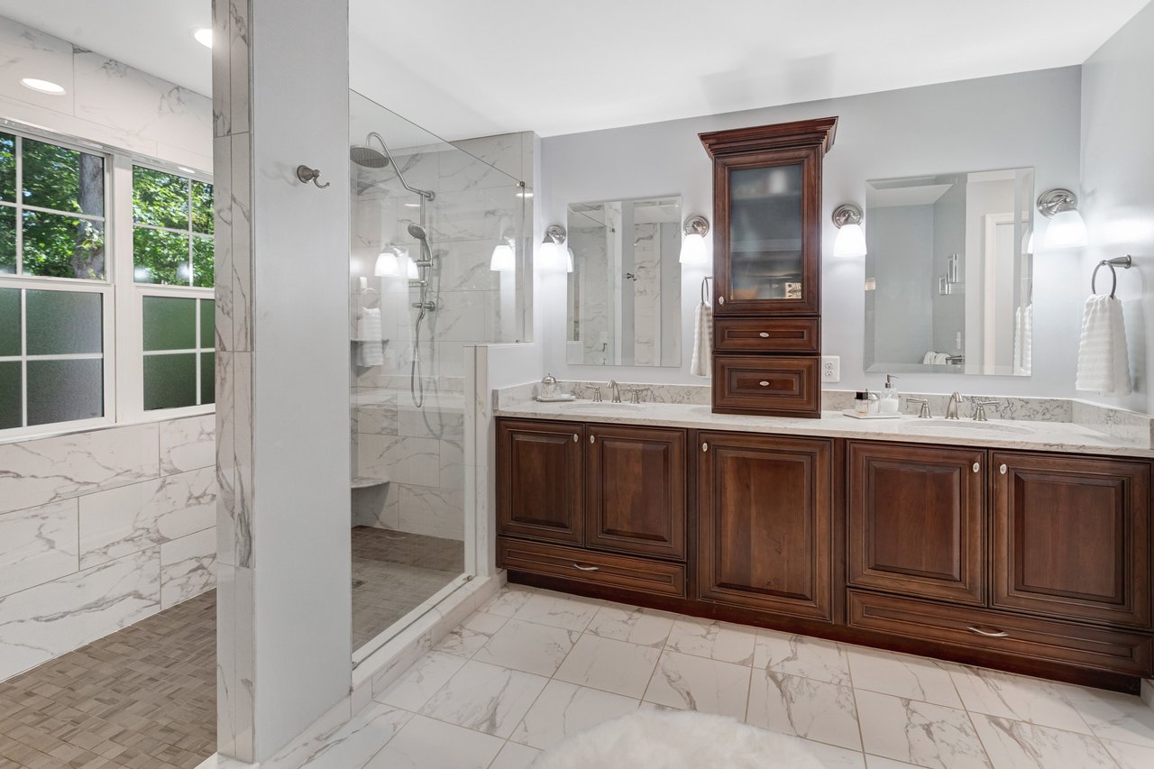 Bathroom with a glass-enclosed marble shower and dark wood double vanity.