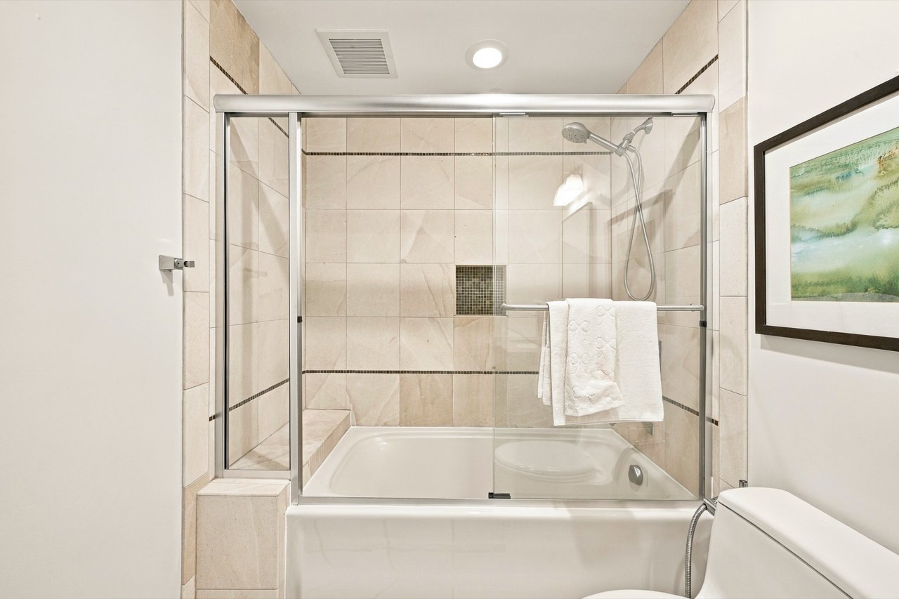 Bathroom with a tiled shower-over-tub, glass enclosure, and white towels.