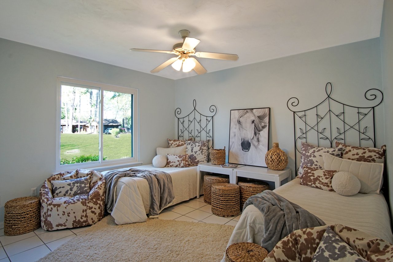 Cozy bedroom with twin beds adorned in cowhide-patterned pillows, cream throws, and wicker baskets. A serene horse artwork adds a rustic touch. Bright window view.