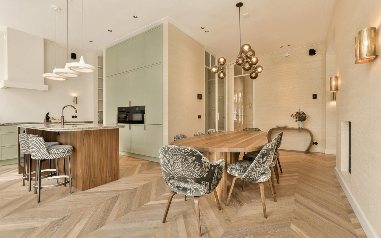 Modern kitchen and dining area with pale green cabinets, a wood-paneled island, and herringbone flooring.