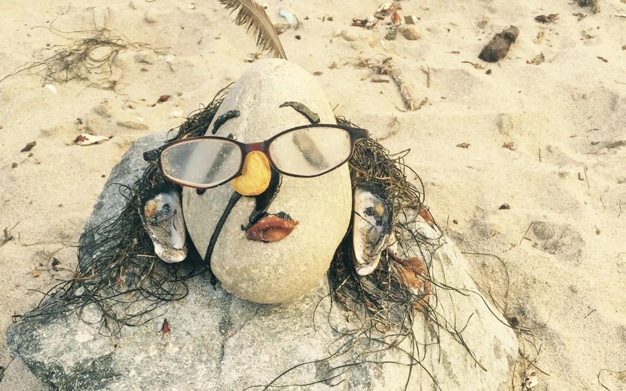 A beach sculpture made from stones and seaweed, with glasses forming a face.