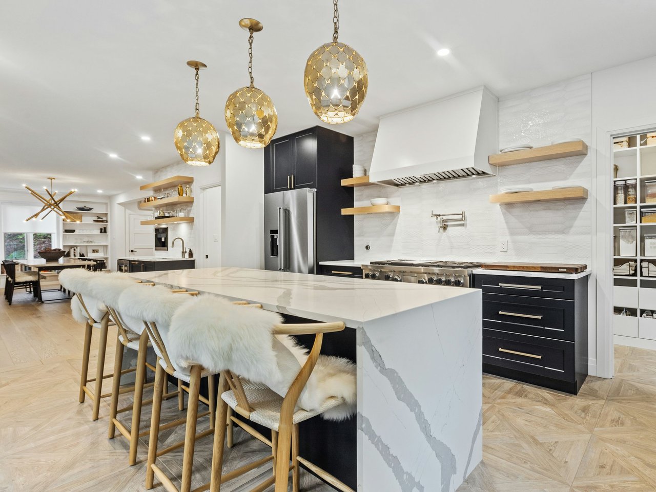 Open-plan kitchen with a marble waterfall island, dark cabinets, and three gold pendant lights.