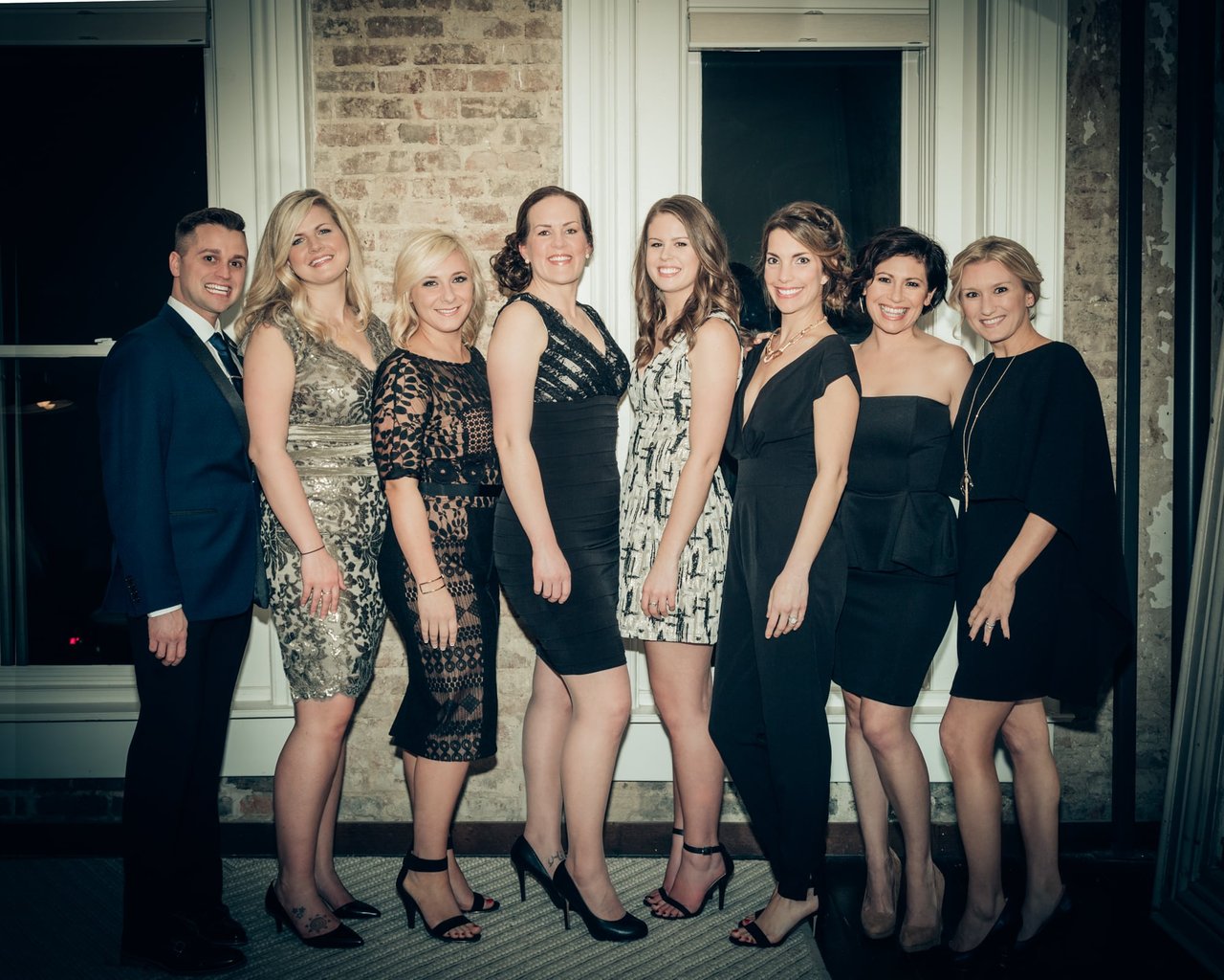 Nine formally dressed adults pose together inside a venue.