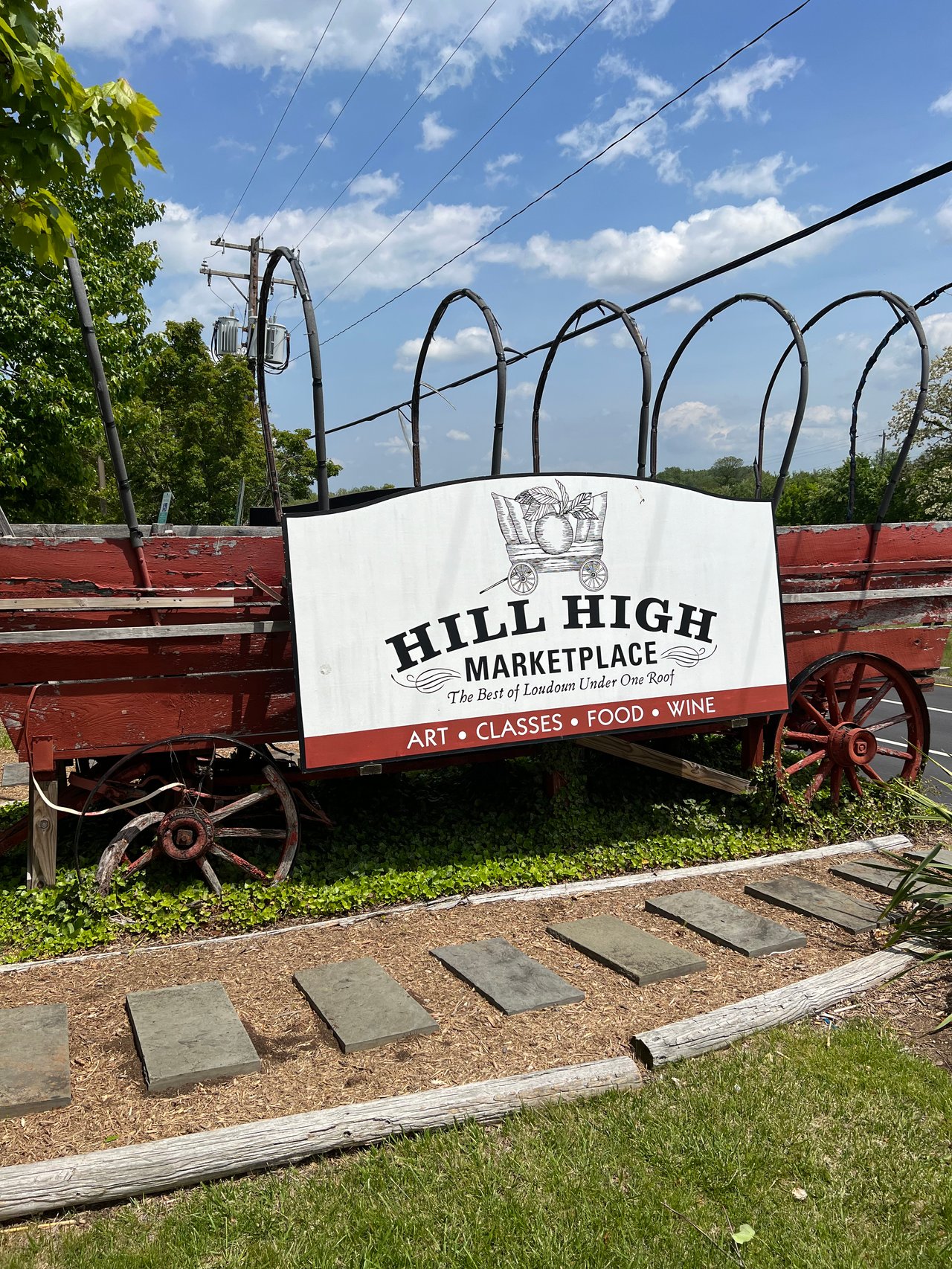 Hill High Marketplace sign mounted on a vintage red covered wagon in Round Hill, Virginia, reading "The Best of Loudoun Under One Roof — Art, Classes, Food, Wine"