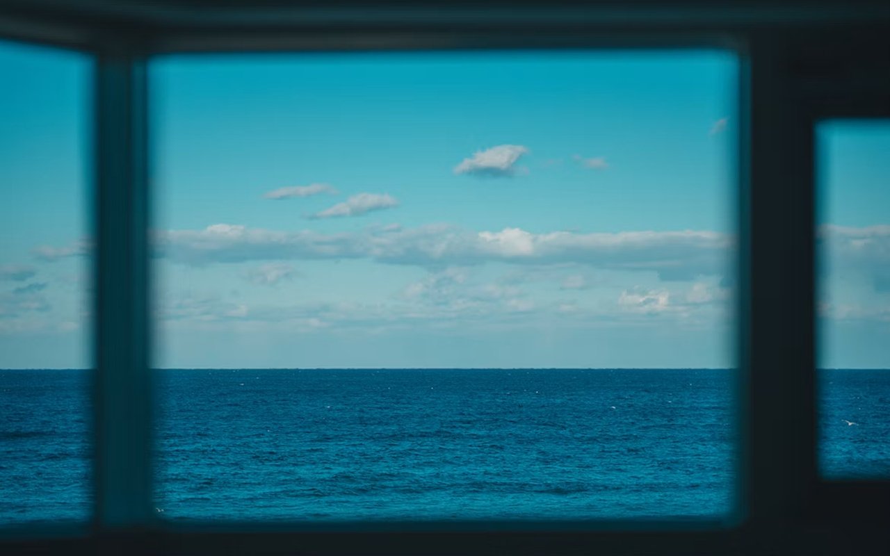 Blue ocean and cloudy sky framed by a dark window
