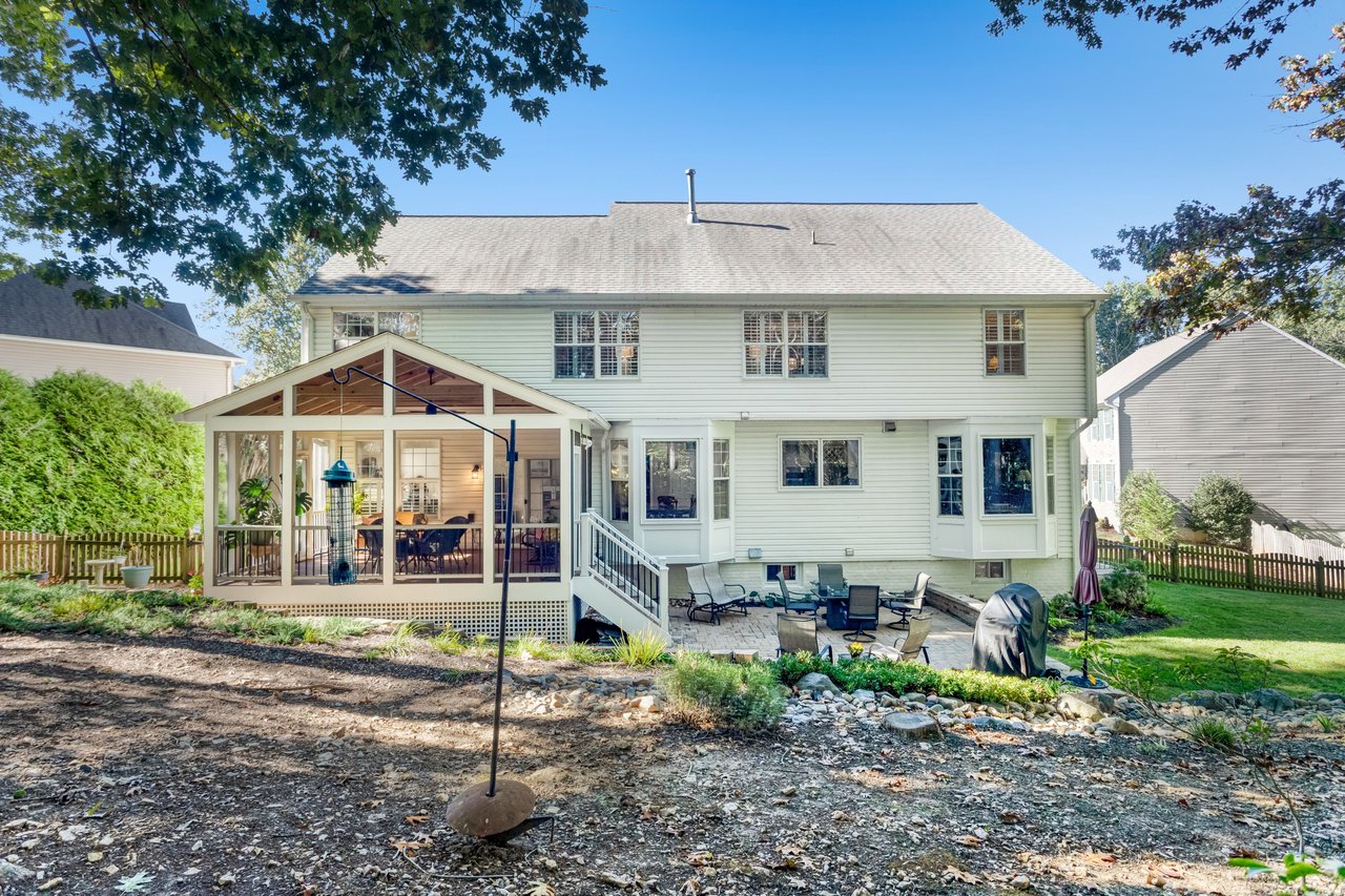 Rear exterior of a two-story home with a screened porch and stone patio.