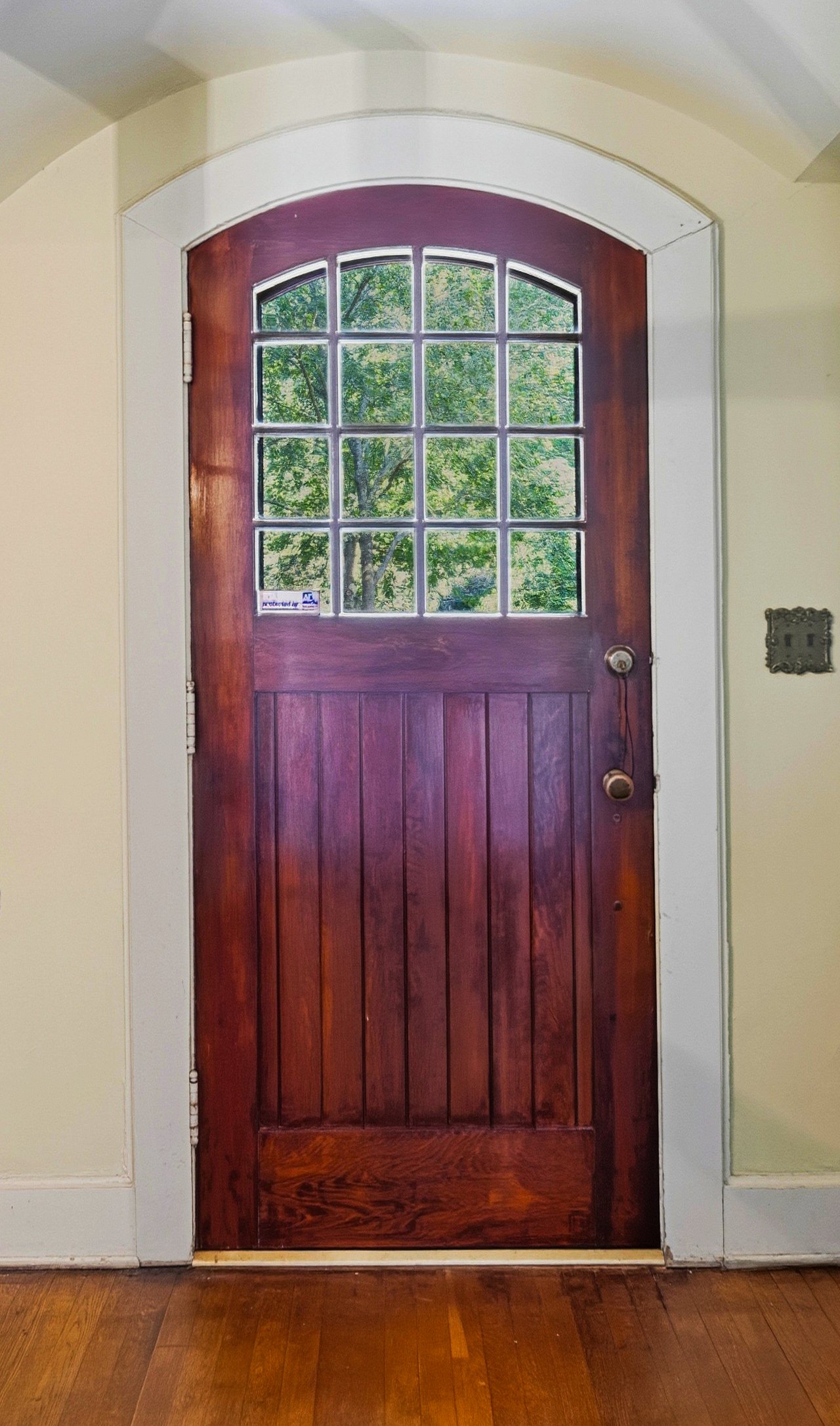 Arched wooden entry door with divided glass panes, cream walls, and hardwood flooring.
