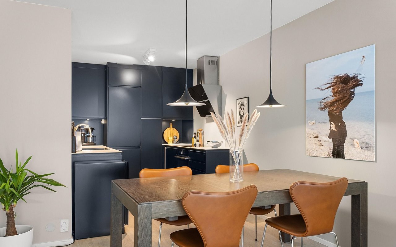 Modern kitchen and dining area with navy cabinets, a wood table, tan chairs, and pendant lights.