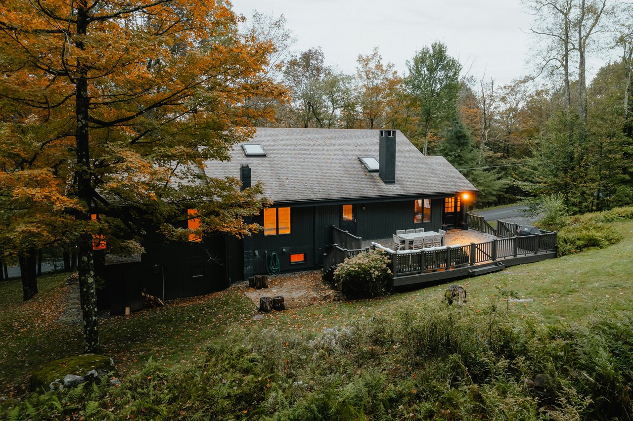 Dark modern house with a furnished deck among autumn trees on a wooded slope.