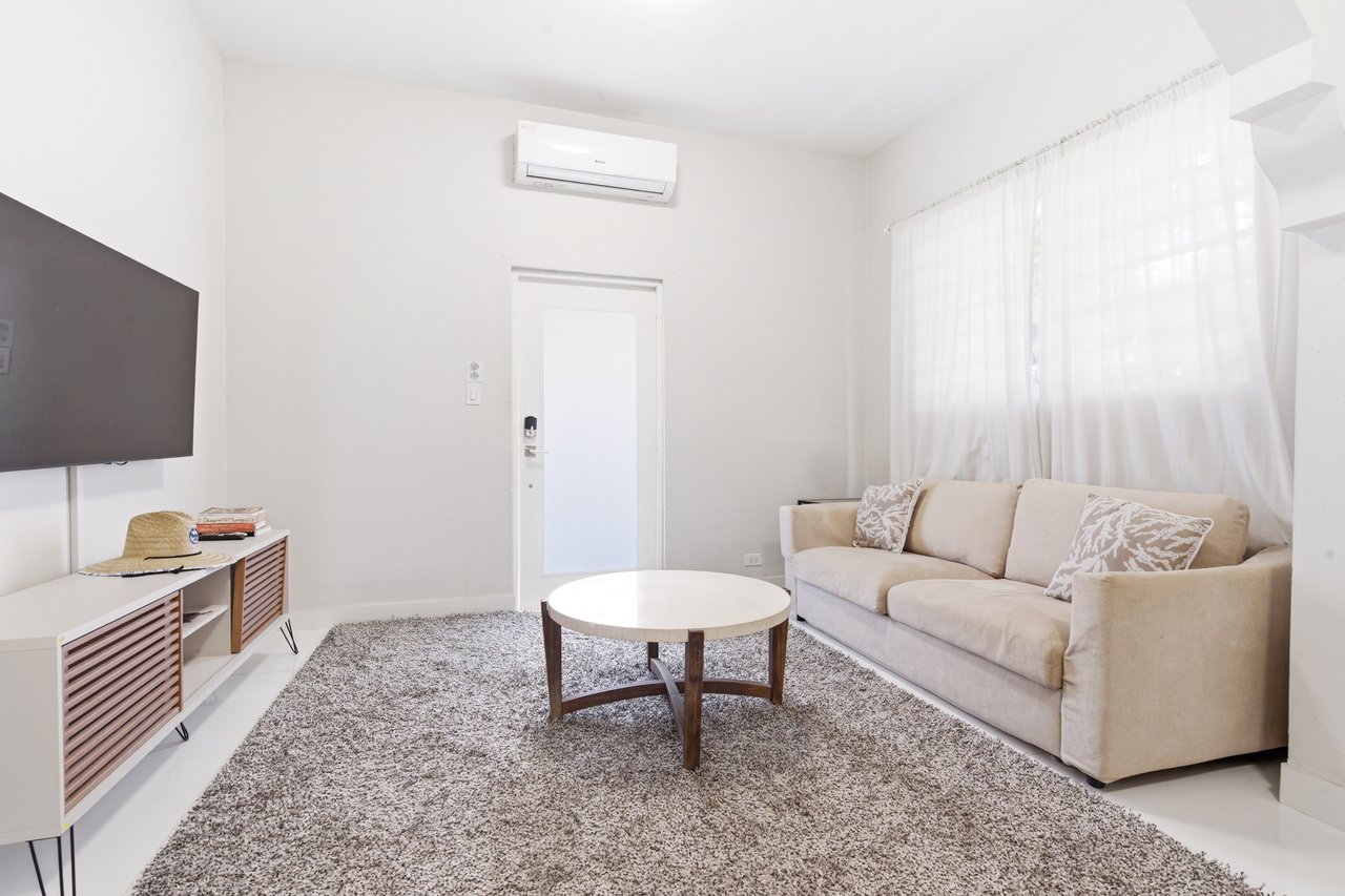 Furnished living room with a beige sofa, round coffee table, and sheer-curtained windows.
