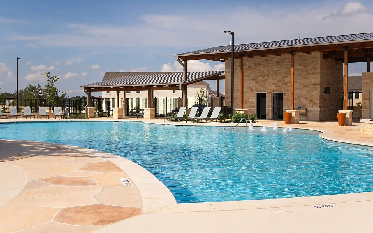 Community pool beside stone pavilion buildings and lounge chairs.