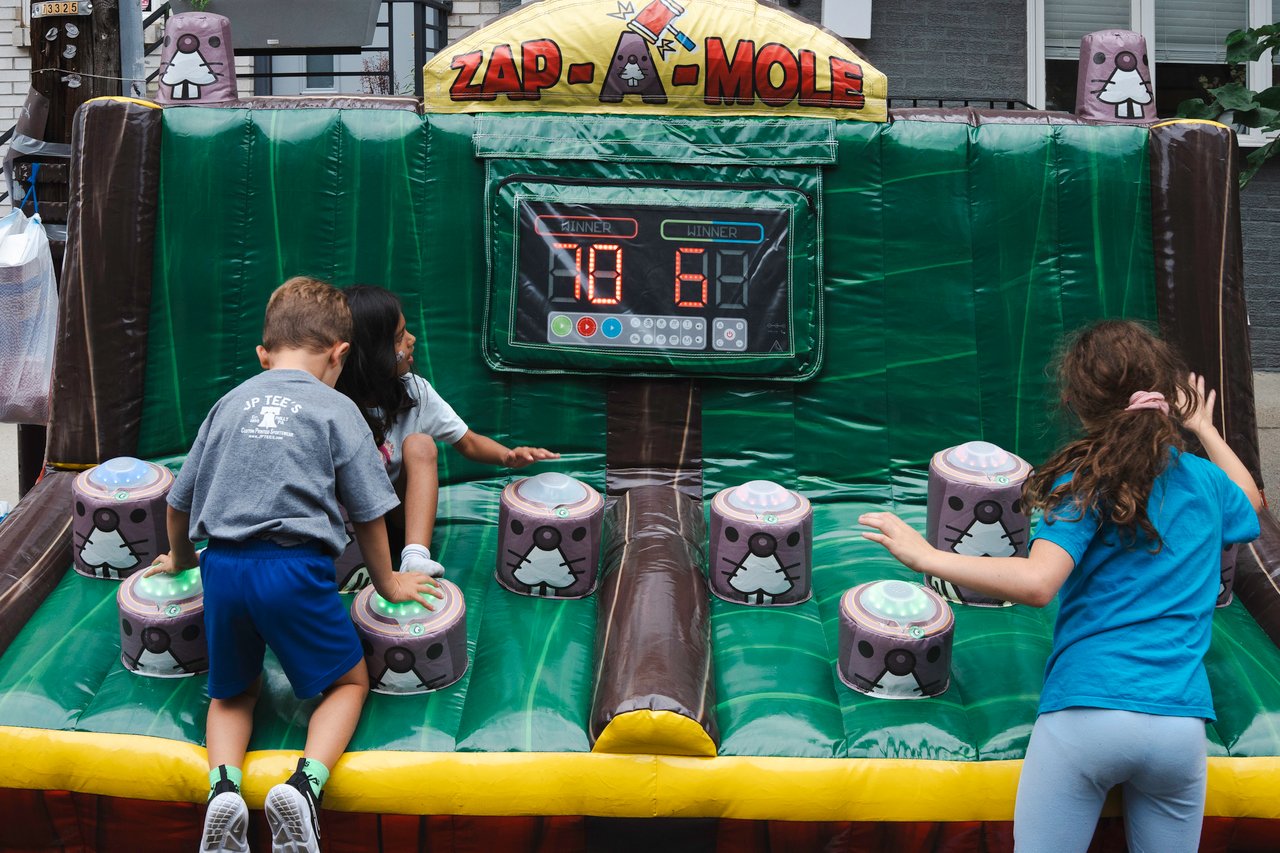 Children play a green Zap-A-Mole inflatable game with mole-shaped targets.