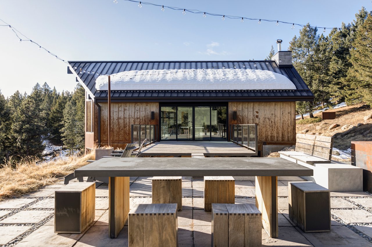 Modern outdoor dining area with concrete table and wood block seating against Boulder mountain home backdrop