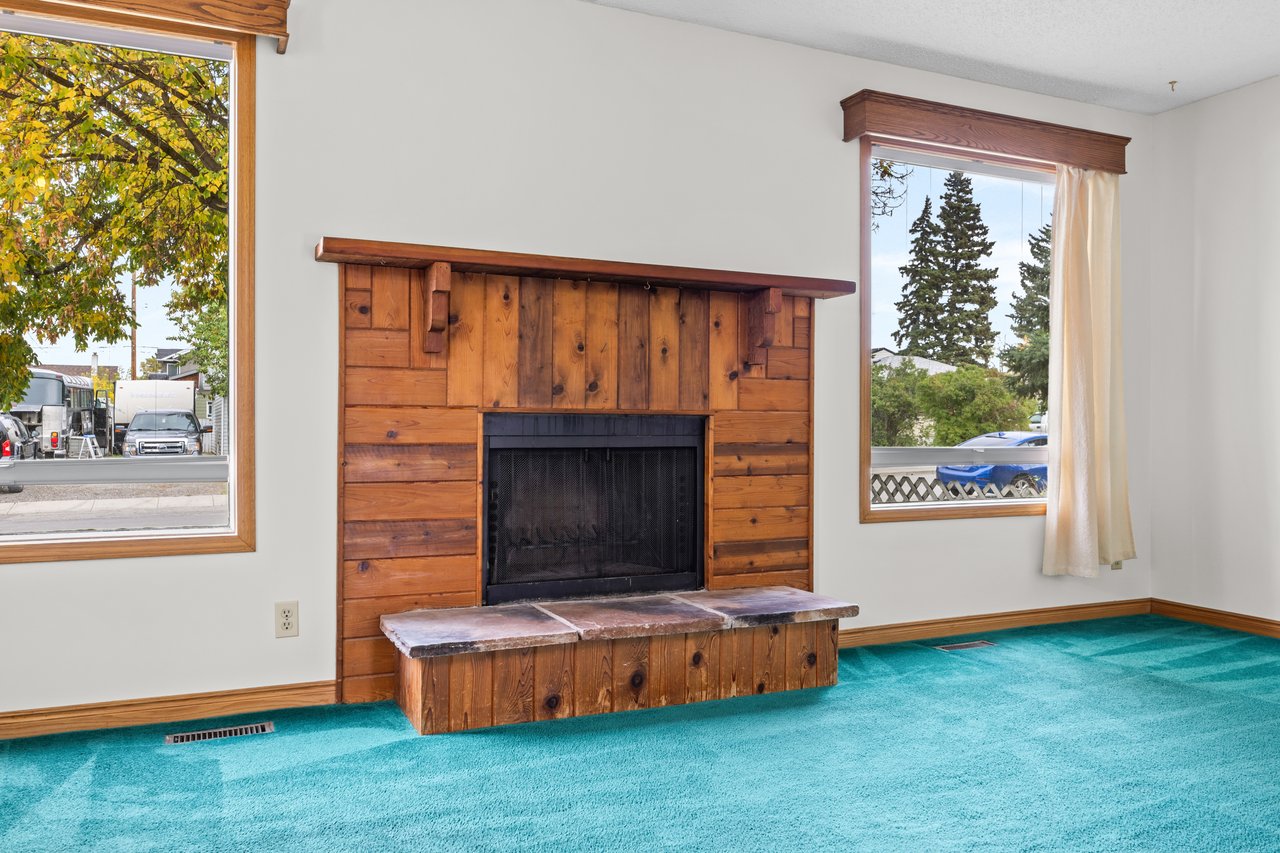 Unfurnished living room with a rustic wood fireplace and bright turquoise carpet.