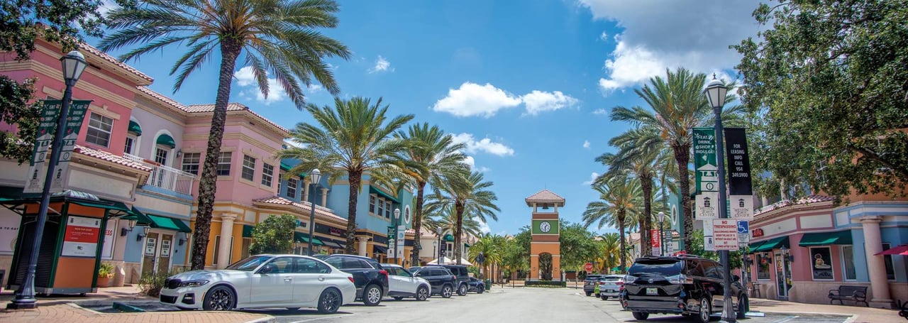 Colorful storefronts and palm-lined street leading to clock tower at Weston Town Center in Florida.