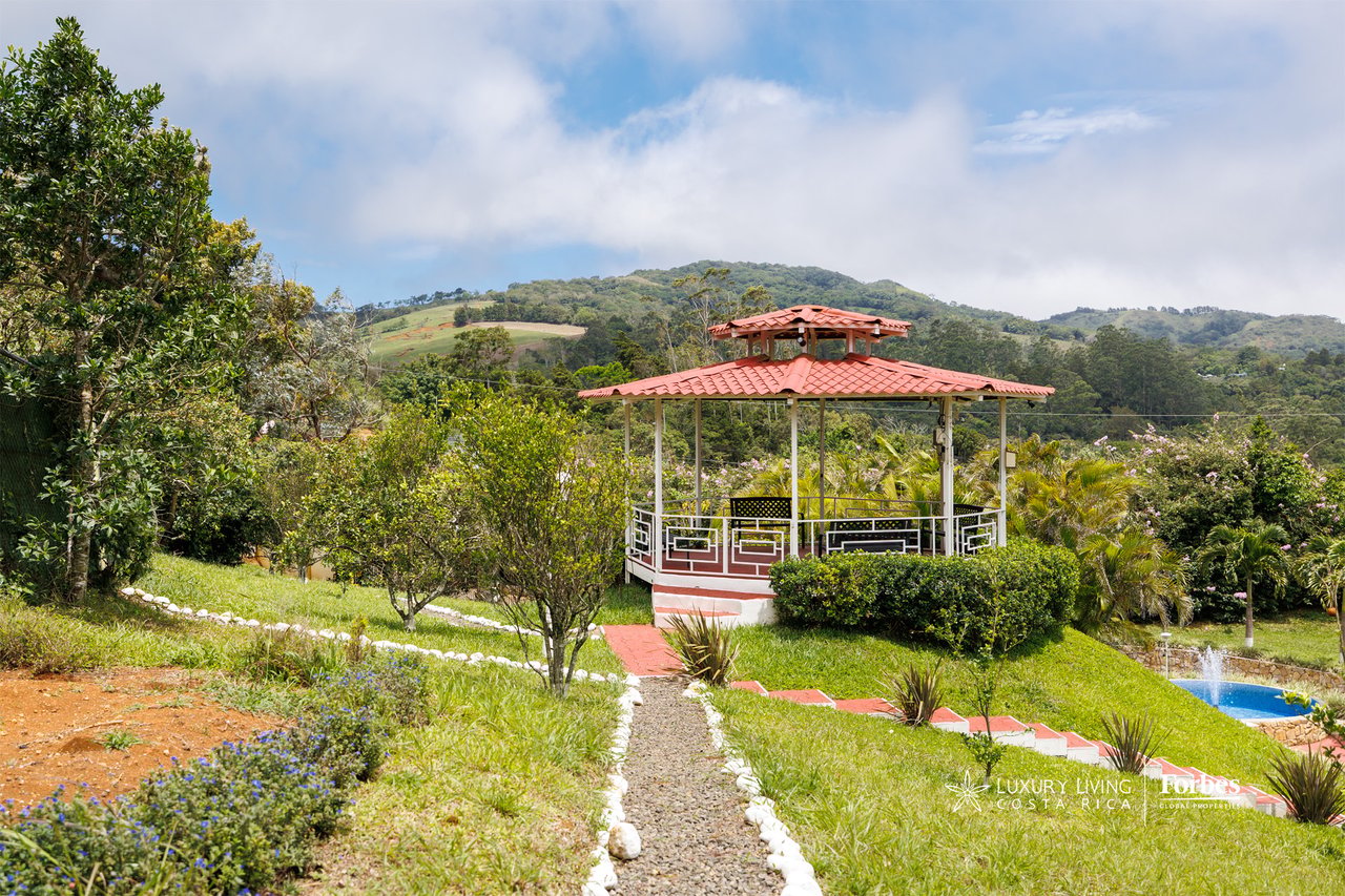 Garden gazebo with a red tile roof, stone path, small pool, and green mountain views.