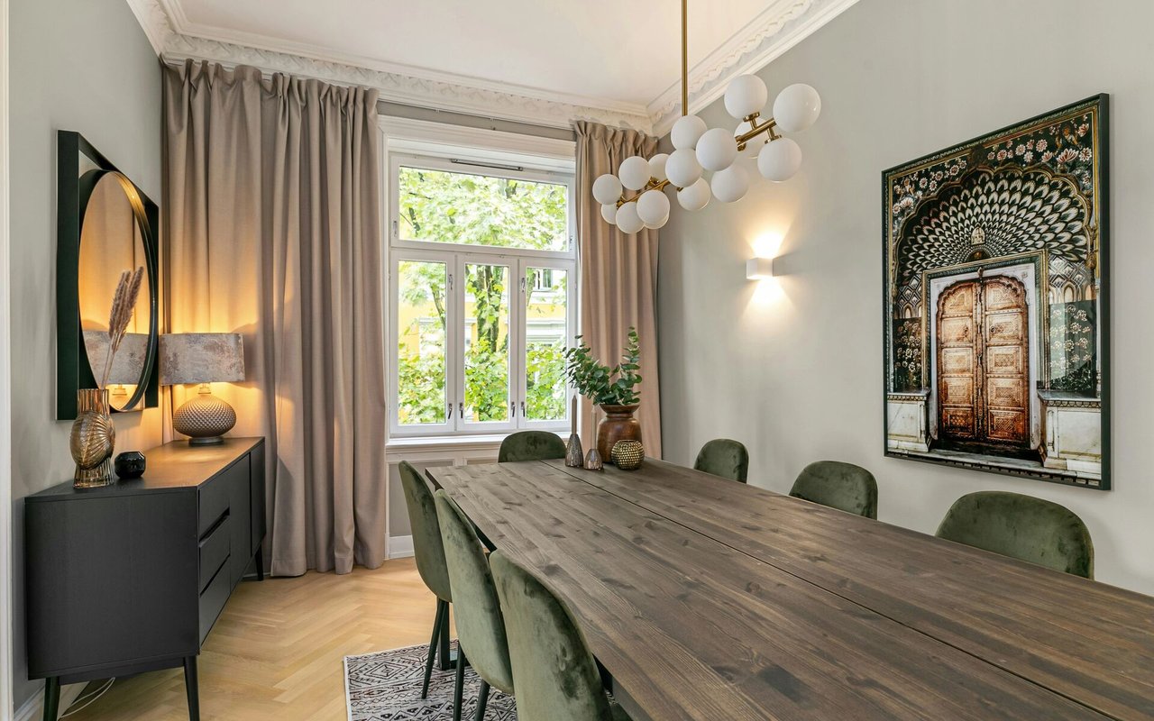 Dining room with a long wood table, green chairs, and a large curtained window.