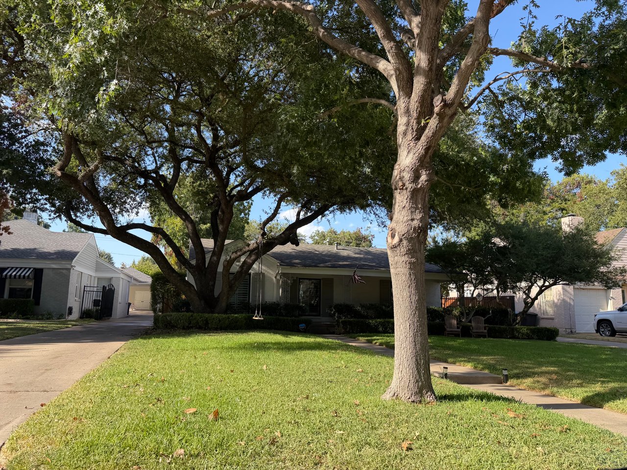 Single-story home shaded by mature oak trees, with a broad front lawn and driveway.