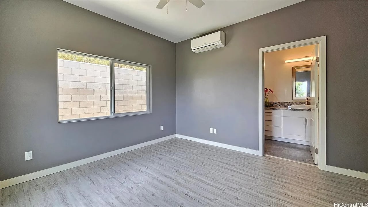 Empty bedroom with gray walls, plank flooring, and a doorway to a bathroom.