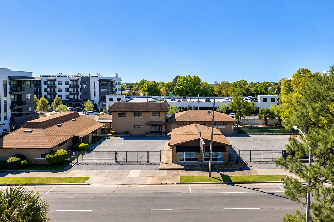 Low-rise property with a fenced parking lot, seen from above beside a road.