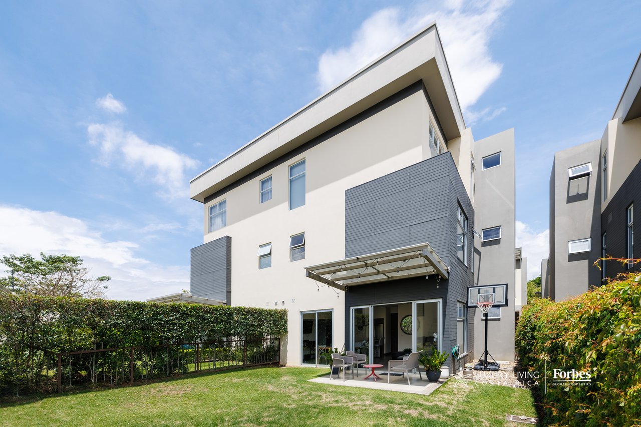 Modern townhouse with a hedge-lined garden, covered patio, outdoor seating, and basketball hoop.