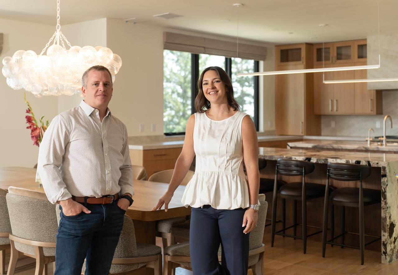 Two real estate agents stand beside a dining table in a modern kitchen.