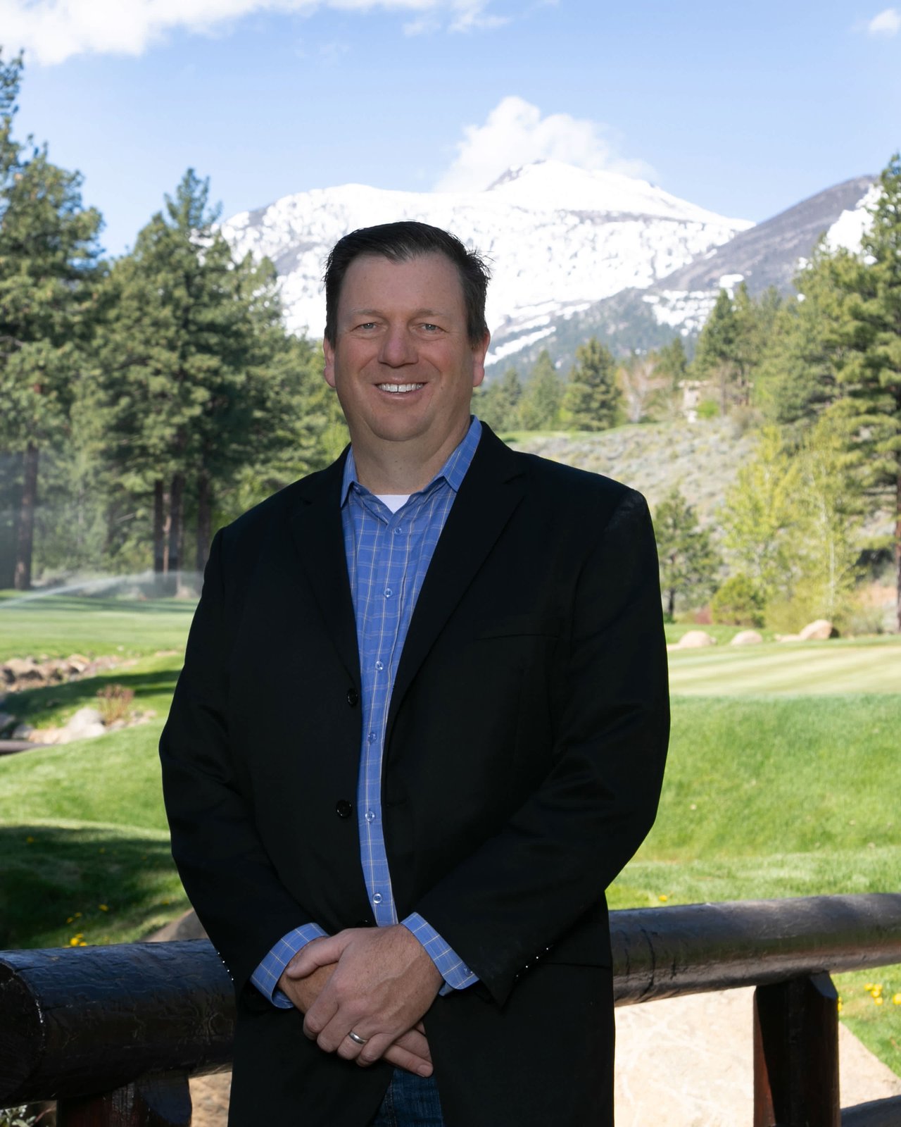 Michael Herman, Montreux luxury real estate agent, standing outdoors in front of a scenic golf course and snow-capped mountains.