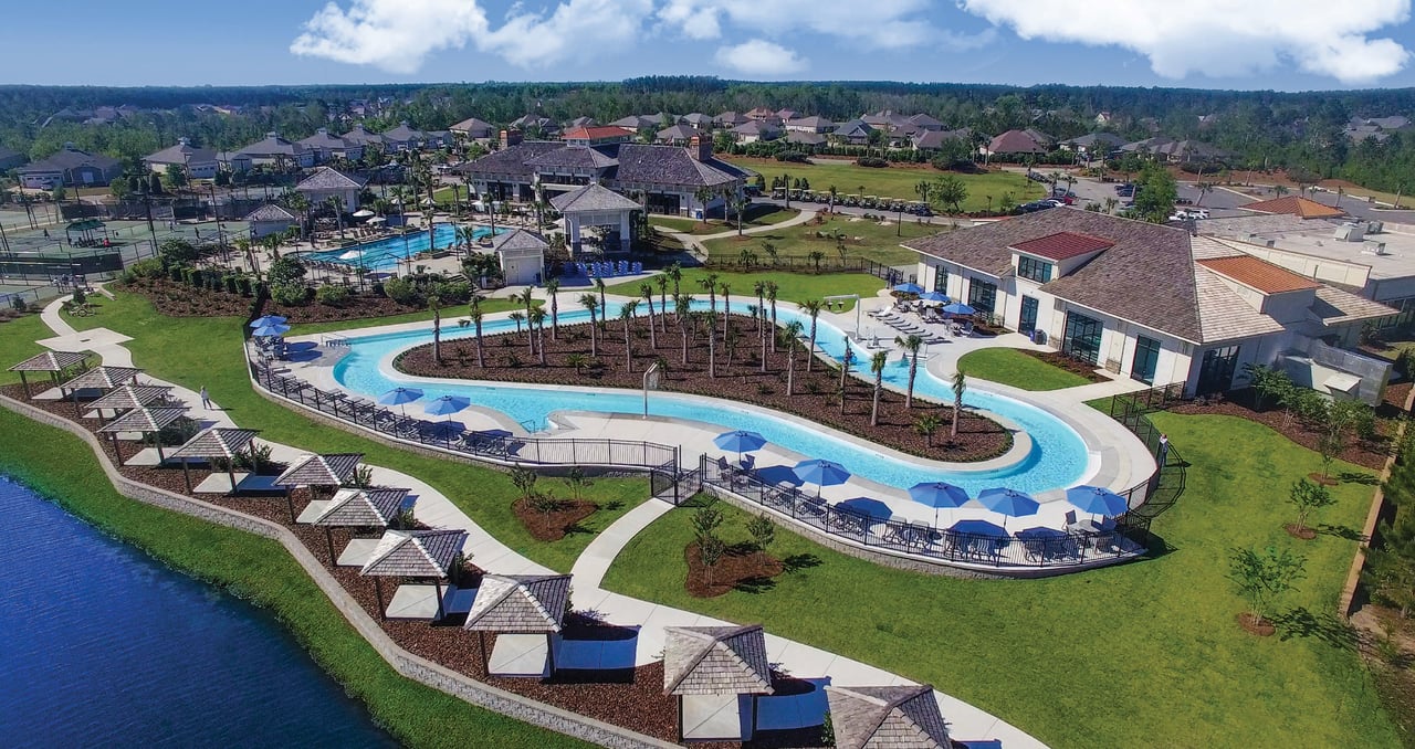 Aerial view of a winding outdoor pool beside the clubhouse and a lakeside walking path.